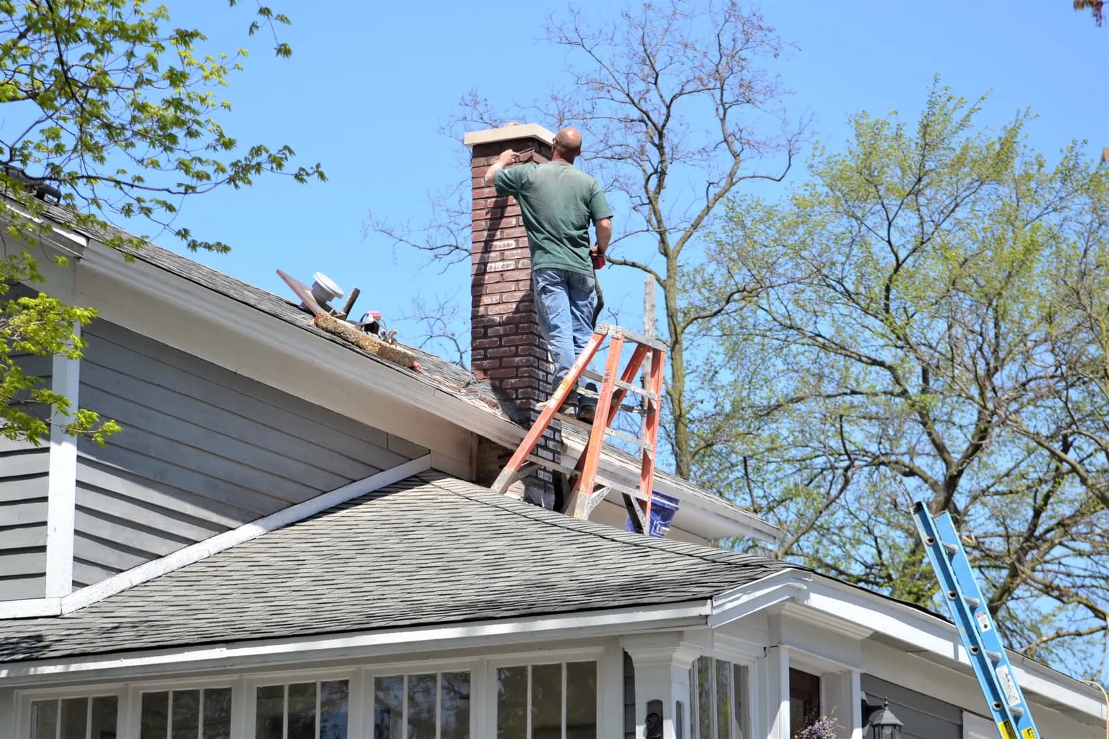 Technician on a ladder working on a brick chimney