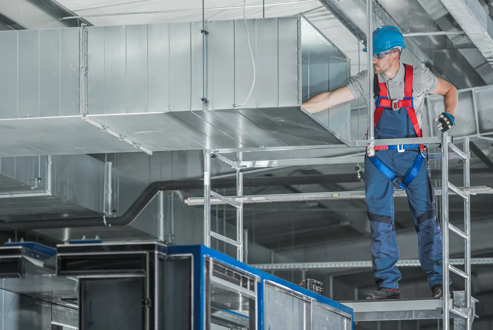 HVAC technician inspecting commercial ventilation ducts from a scaffold