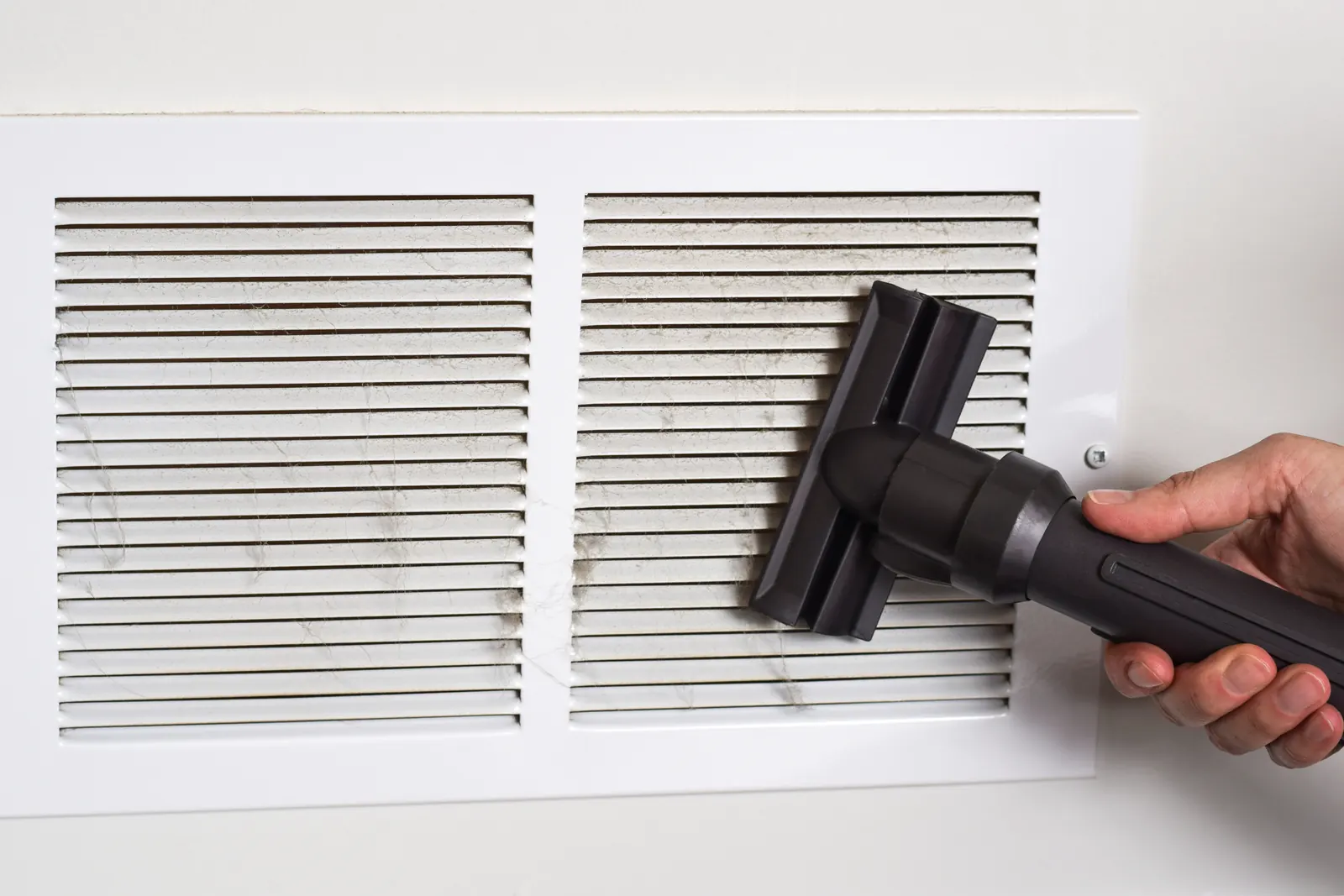 Vacuum hose cleaning dust from a white air vent